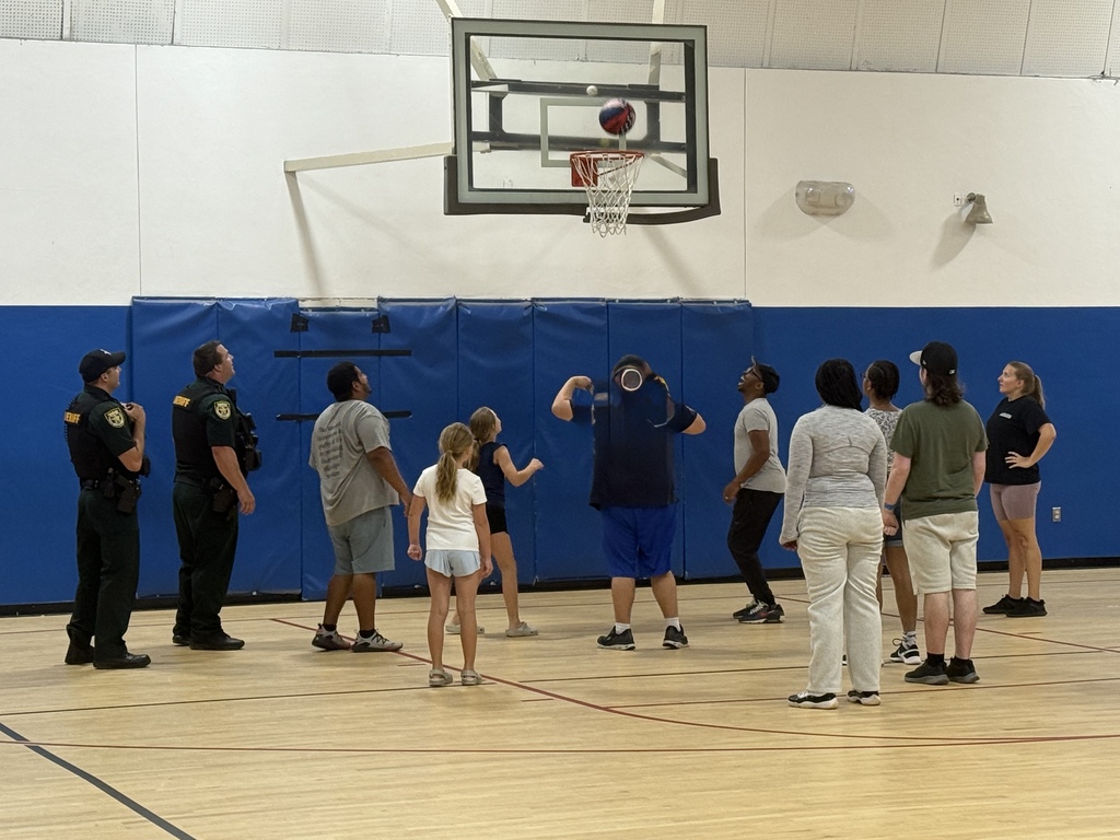 Students, staff members, and school resource officers watch a basketball shot near the hoop during the school basketball game.