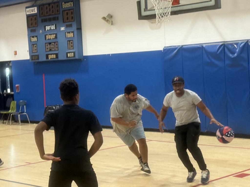 Two participants move down the basketball court while other students watch and prepare to play during the annual basketball game.