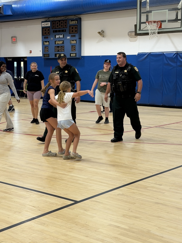 Two school resource officers interact with students on the basketball court during the annual staff versus student basketball game.