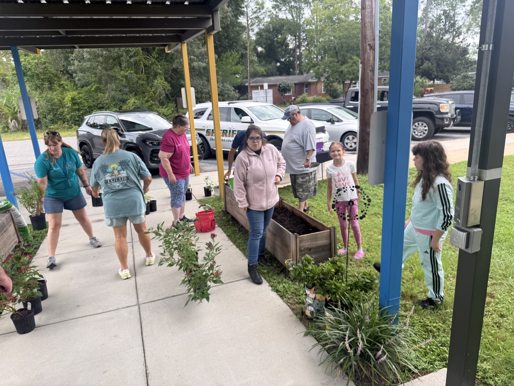 Richbourg students and adults work together outdoors to prepare raised garden beds and arrange plants for planting on the school campus.