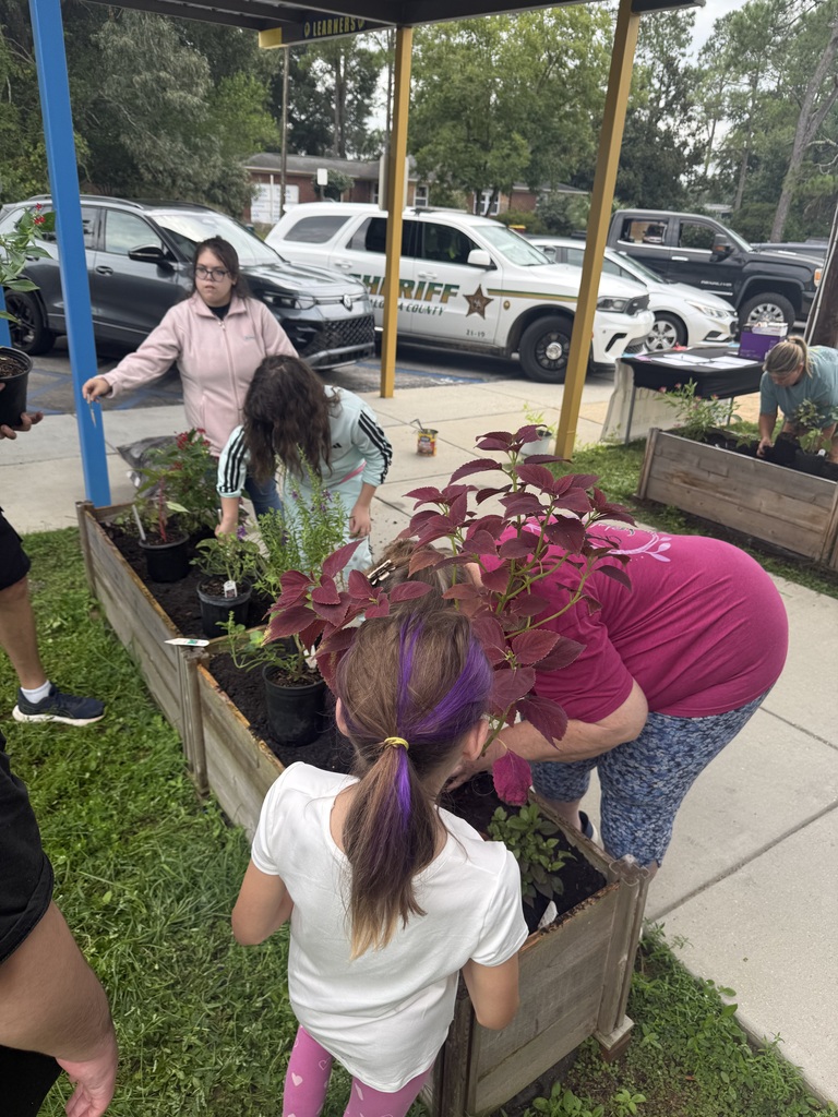 Richbourg students and adults work together outdoors to prepare raised garden beds and arrange plants for planting on the school campus.
