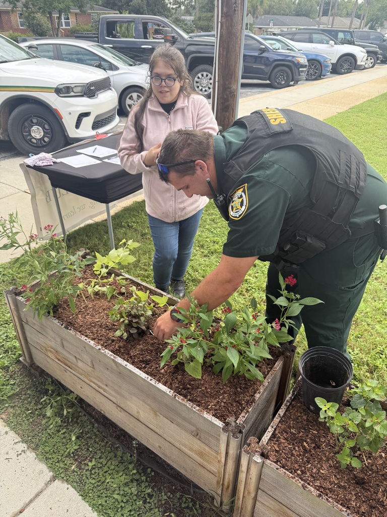 A Richbourg student watches as a Richbourg's resource officer helps plant colorful flowers in a raised garden bed on the school campus.