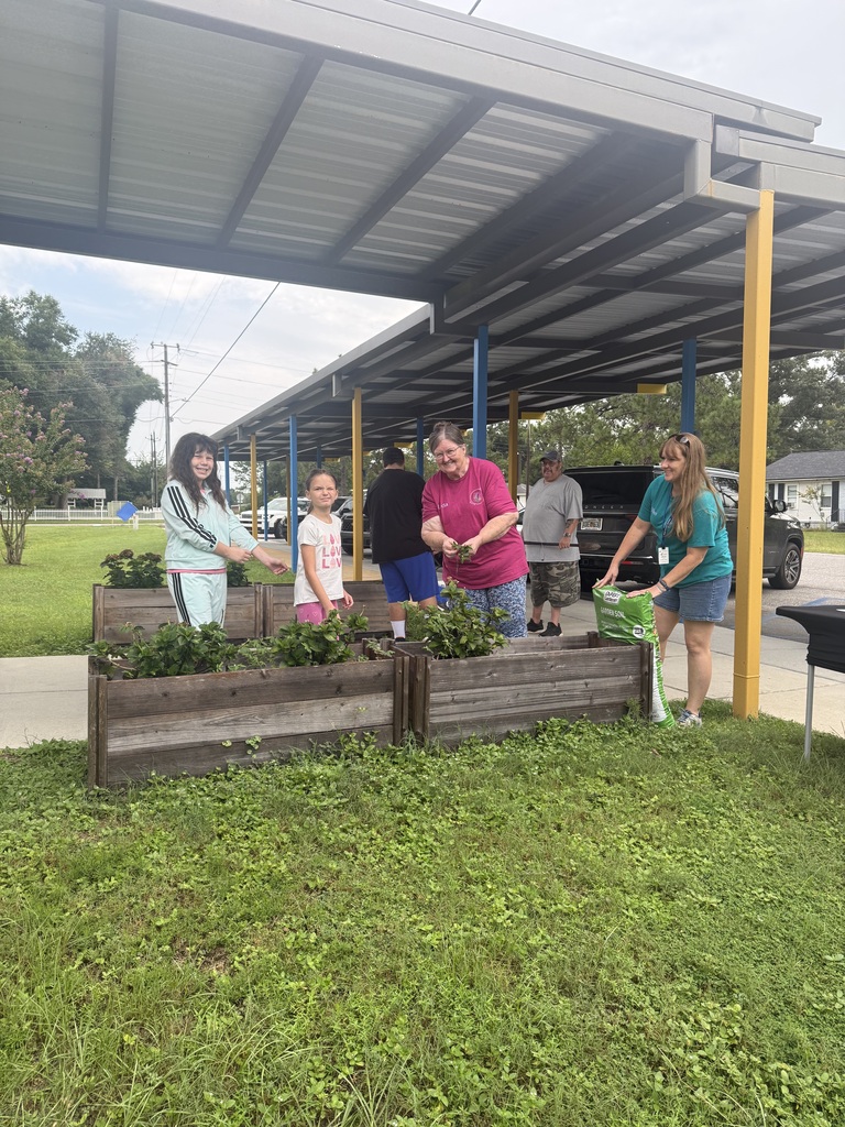 Richbourg students work alongside adults to plant and care for greenery in raised garden beds during a hands-on gardening activity on the school campus.