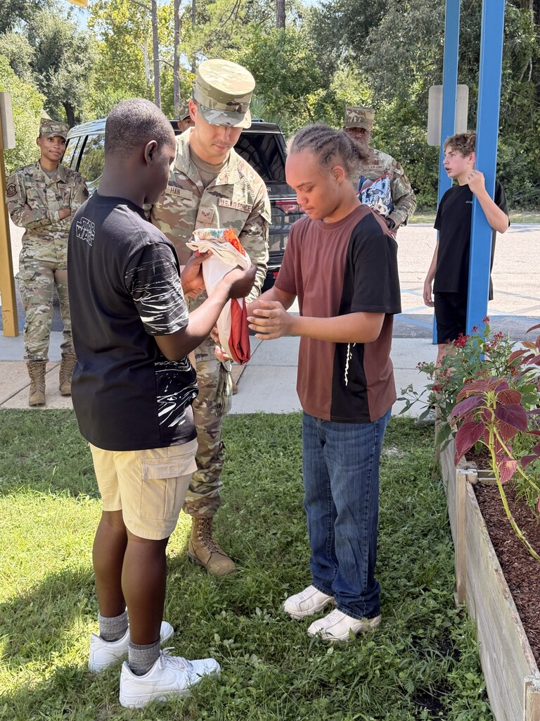 “Richbourg students practice folding the Florida state flag with guidance from a member of the Eglin Air Force Base Honor Guard while other Honor Guard members observe.”
