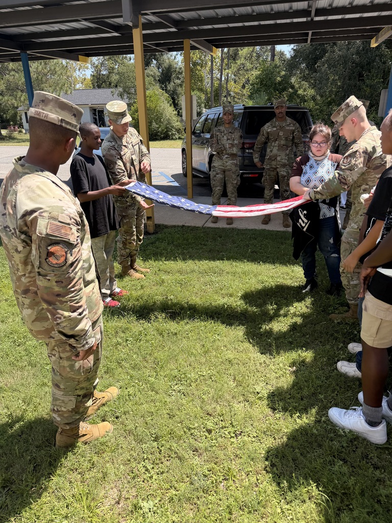 “Richbourg students practice properly folding the American flag with guidance from members of the Eglin Air Force Base Honor Guard during an outdoor demonstration.”