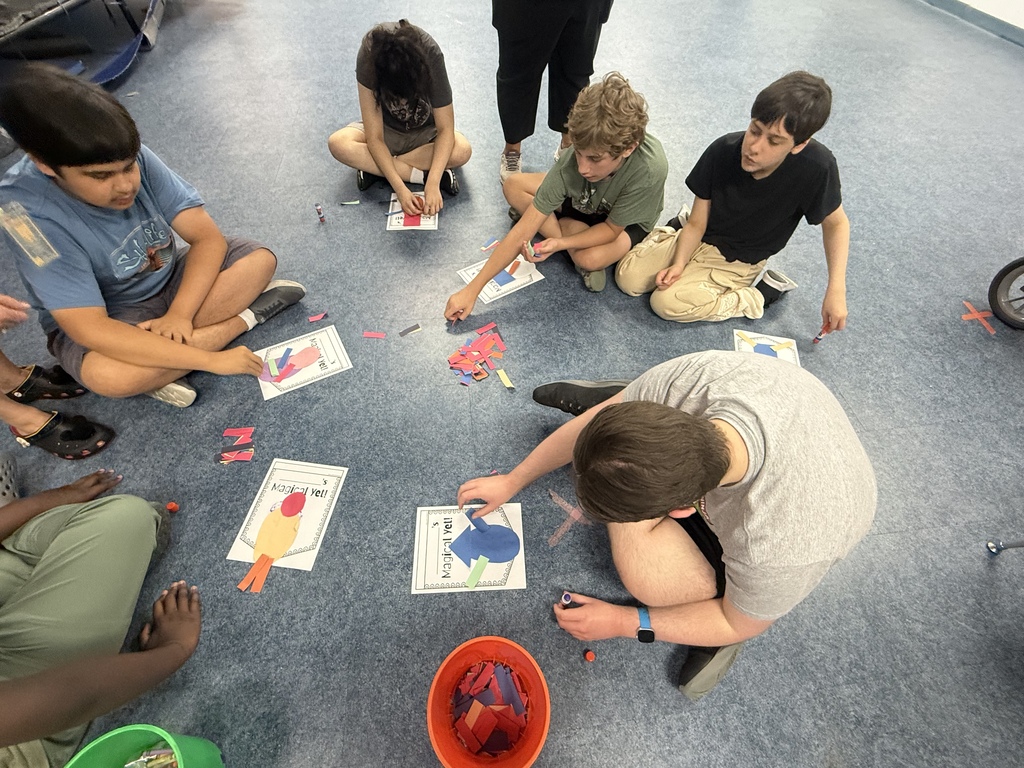 Students sit in a circle on the classroom floor creating “Magical Yet” projects with colorful paper pieces and glue. The hands-on activity encourages creativity while teaching students about resilience, perseverance, and the power of a growth mindset.