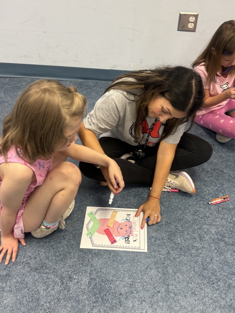 A student and an adult sit on the classroom floor working together on a “Magical Yet” art project. The activity uses colorful paper shapes, markers, and a worksheet to reinforce lessons about persistence and positive thinking.