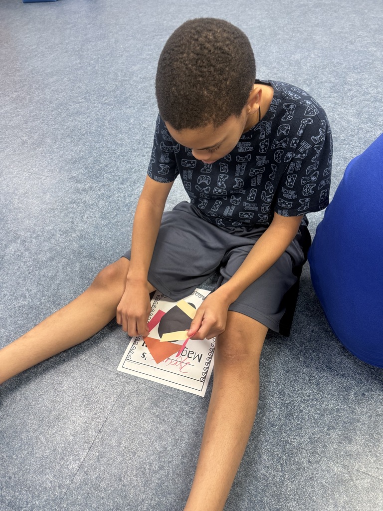 A student sits on the classroom floor creating a "Magical Yet" project using colorful paper shapes. The student arranges pieces on a worksheet inspired by The Magical Yet as part of a hands-on lesson about perseverance, resilience, and developing a growth mindset.