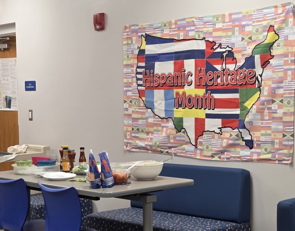 A Hispanic Heritage Month display features a colorful banner with flags and a table of food in a school staff lounge.