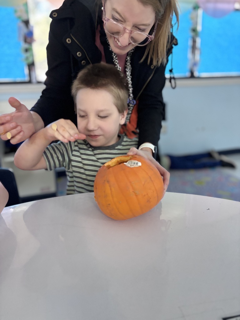 Student examines pumpkin seeds during a hands-on classroom activity while receiving support from an educator.