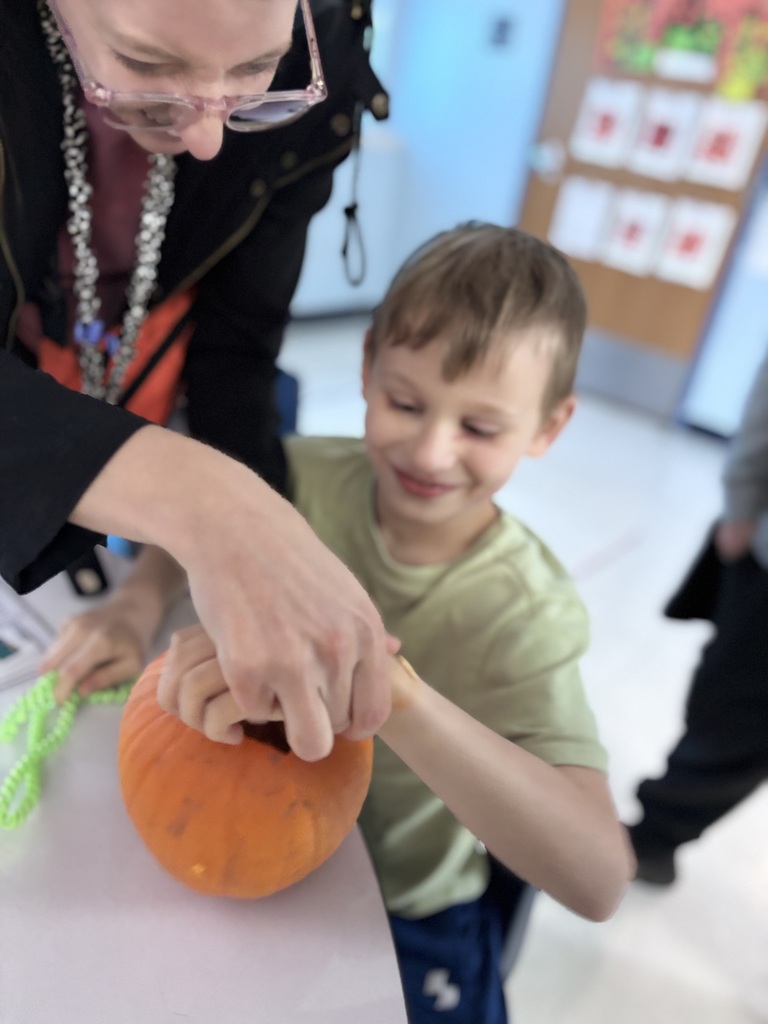 A student participates in a hands-on pumpkin exploration activity, reaching inside a pumpkin with support from an educator. The student explores the texture and contents of the pumpkin during a sensory learning lesson designed to encourage discovery and engagement through touch.