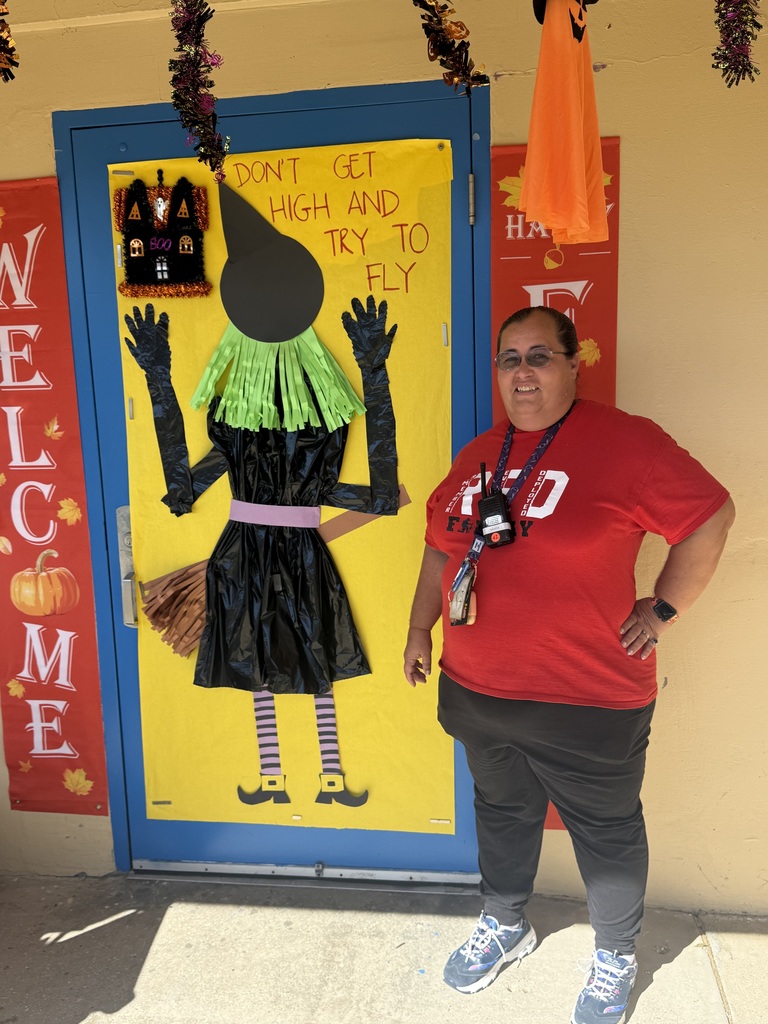 A staff member poses next to a Halloween-themed Red Ribbon Week door decoration featuring a witch and a message encouraging students to make drug-free choices