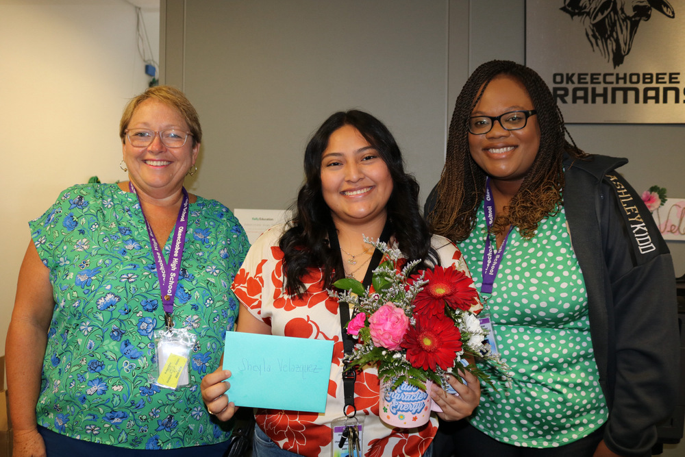 secretary holding flowers next to principal and assistant principal for school related employee of the year