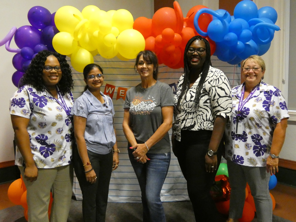 assistant principal and principal standing with three new female teachers Infront of rainbow balloon arch