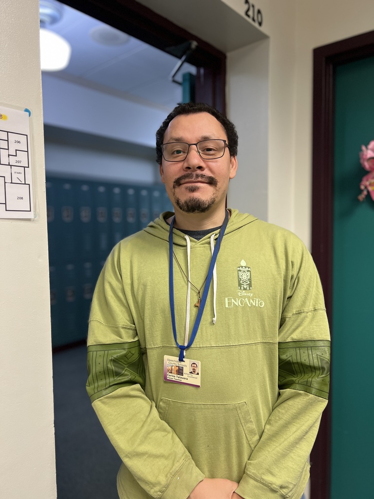 teacher standing by the door wearing green sweatshirt