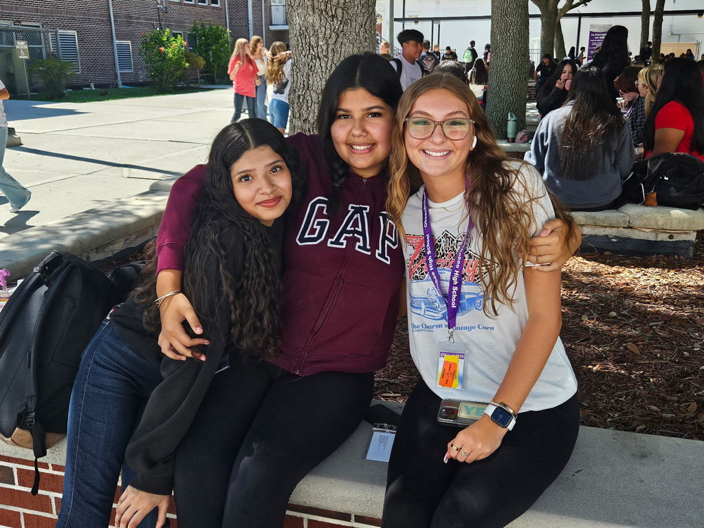 three girls hugging each other in school courtyard