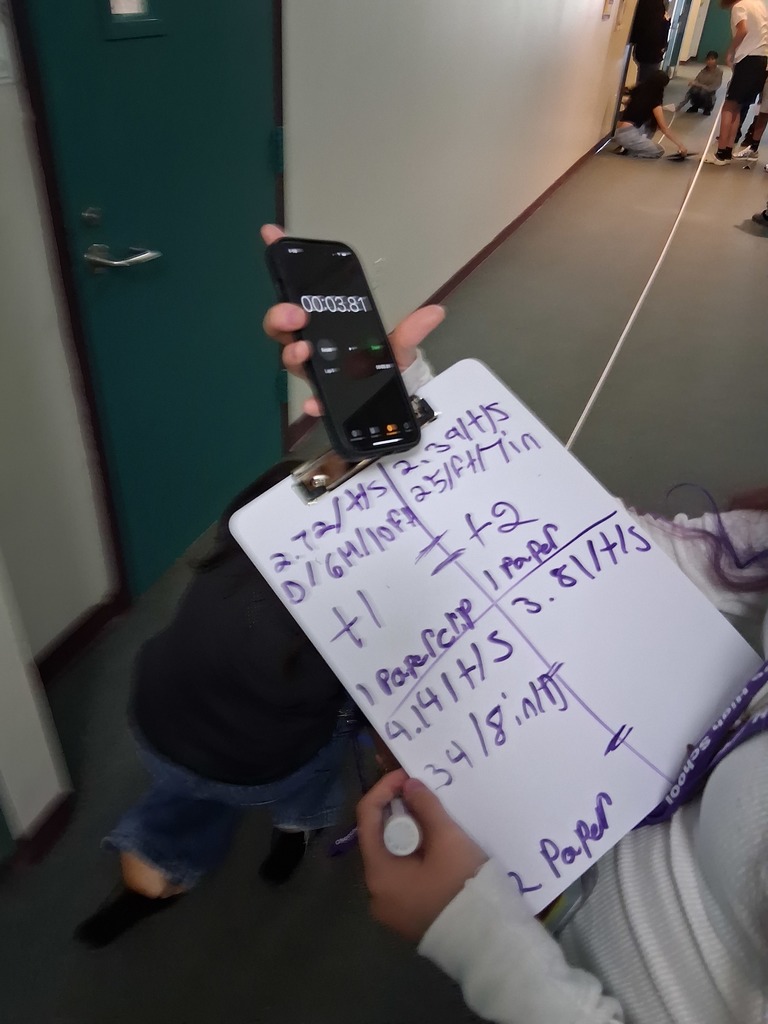 student holding a whiteboard with formulas and a phone standing in hallway 