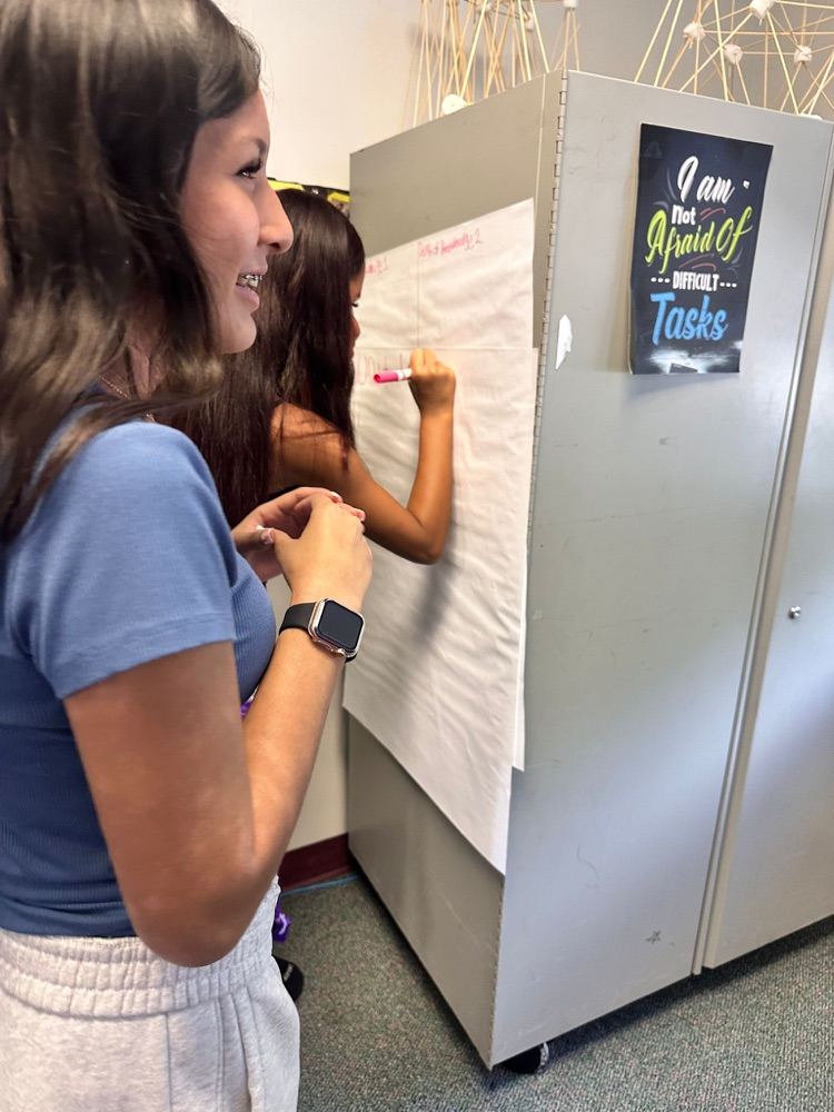side portrait of girl smiling while another writes on poster