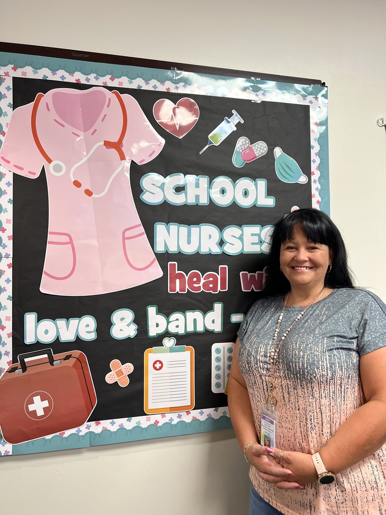nurse aid standing Infront of a wall in her office that reads school nurses heal with love and bandaids