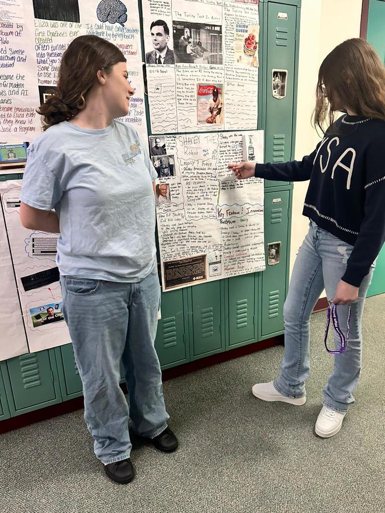 two female students presenting AI poster in hallway