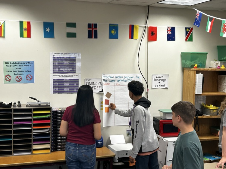 three students sticking post it notes to poster about freedom