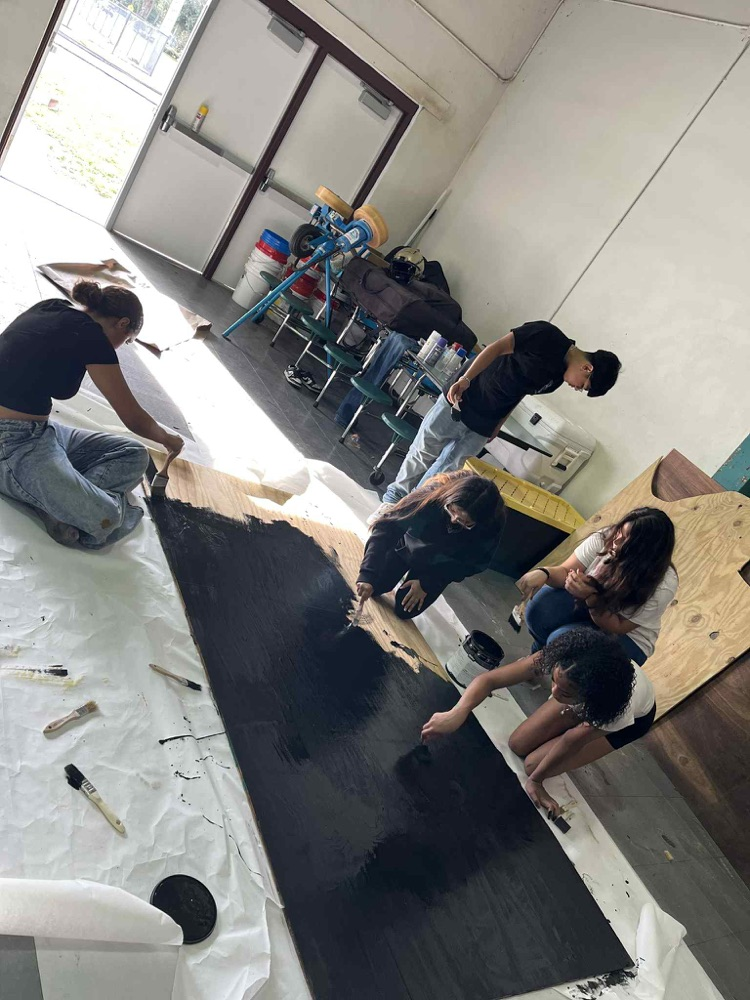 five students painting wood for float building