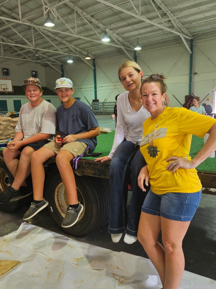 three students and a teacher next to float for parade in gym