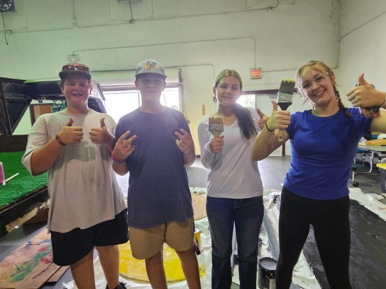 four students showing their brushes for float building in gym