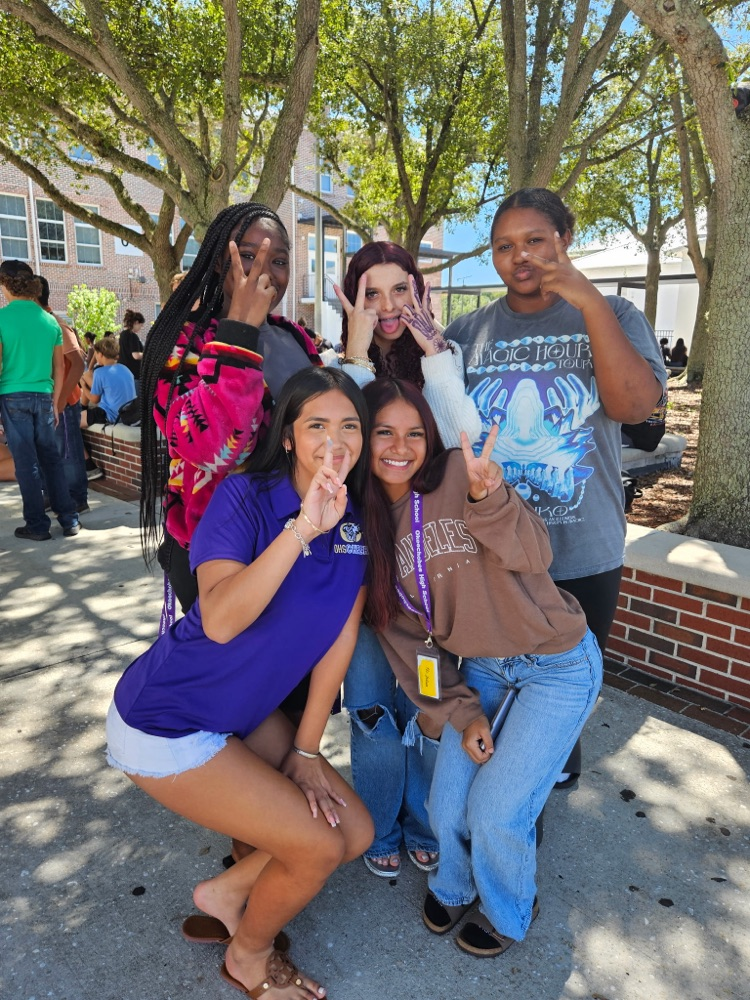 five girls smiling doing hand signs at school lunch courtyard