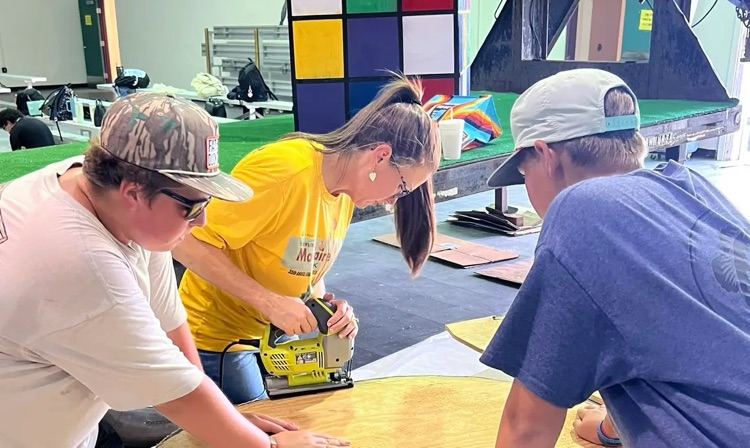 teacher using saw with the help of two students in gym