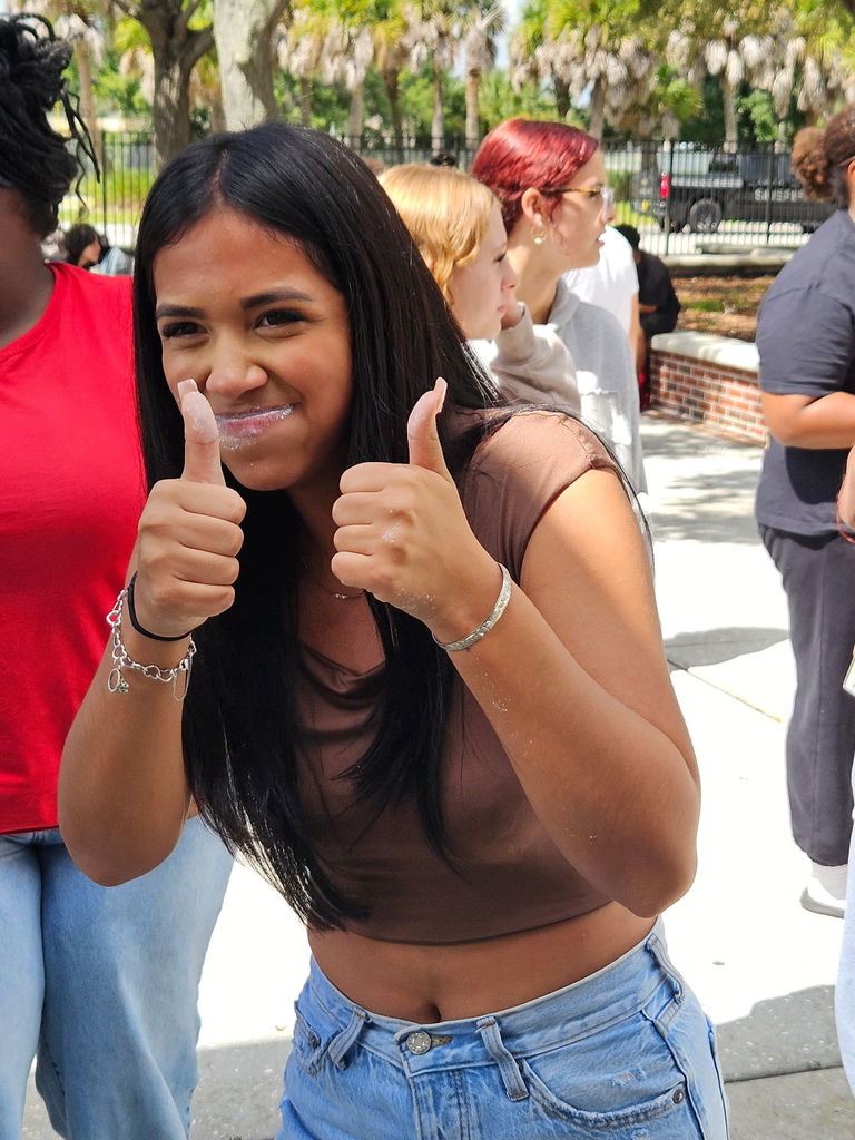 student giving thumbs up outside smiling in school courtyard