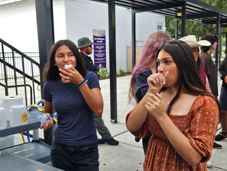 two girls covering mouth stuffing their mouth with doughnuts