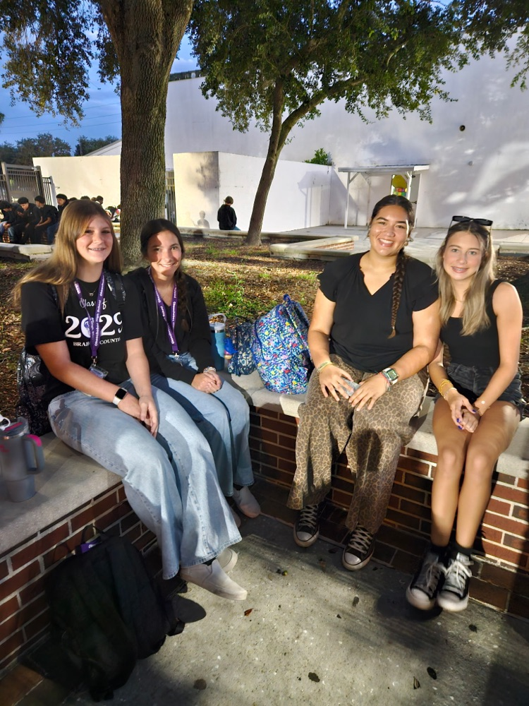 four girls wearing black sitting in school courtyard 