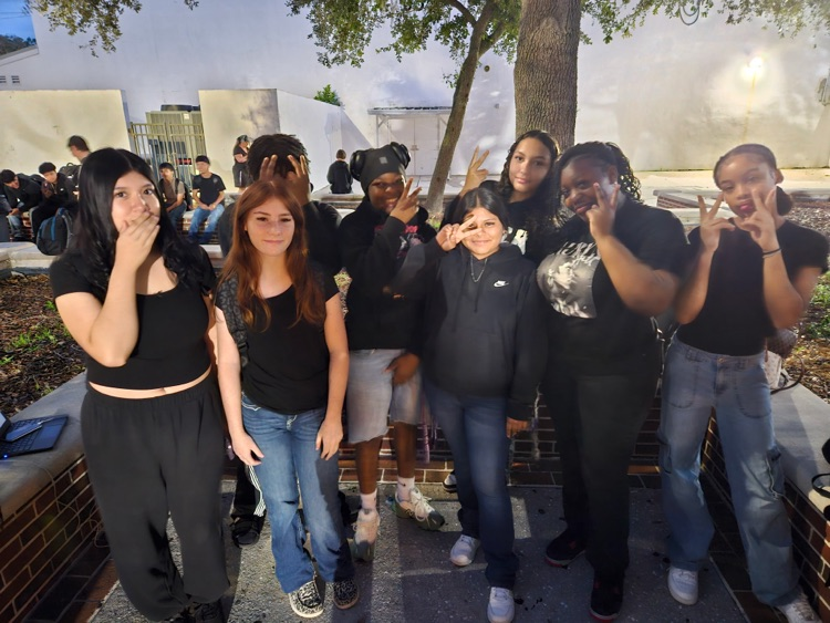 eight students wearing black standing in school courtyard 