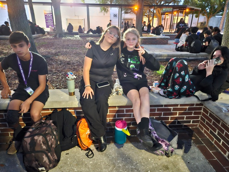 four students wearing black sitting in school courtyard 