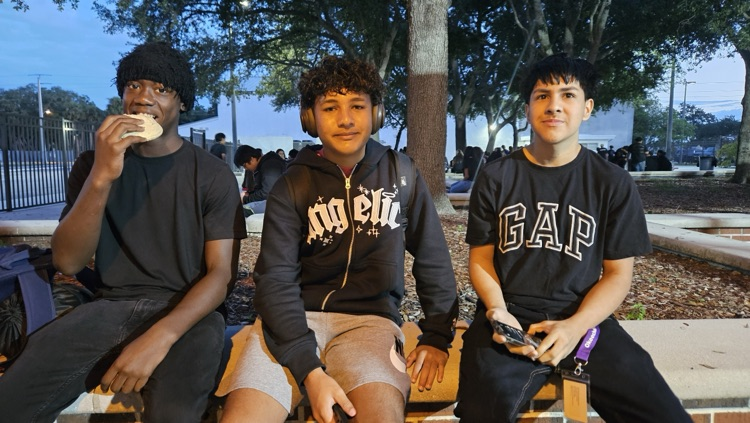 three students wearing black sitting in courtyard 