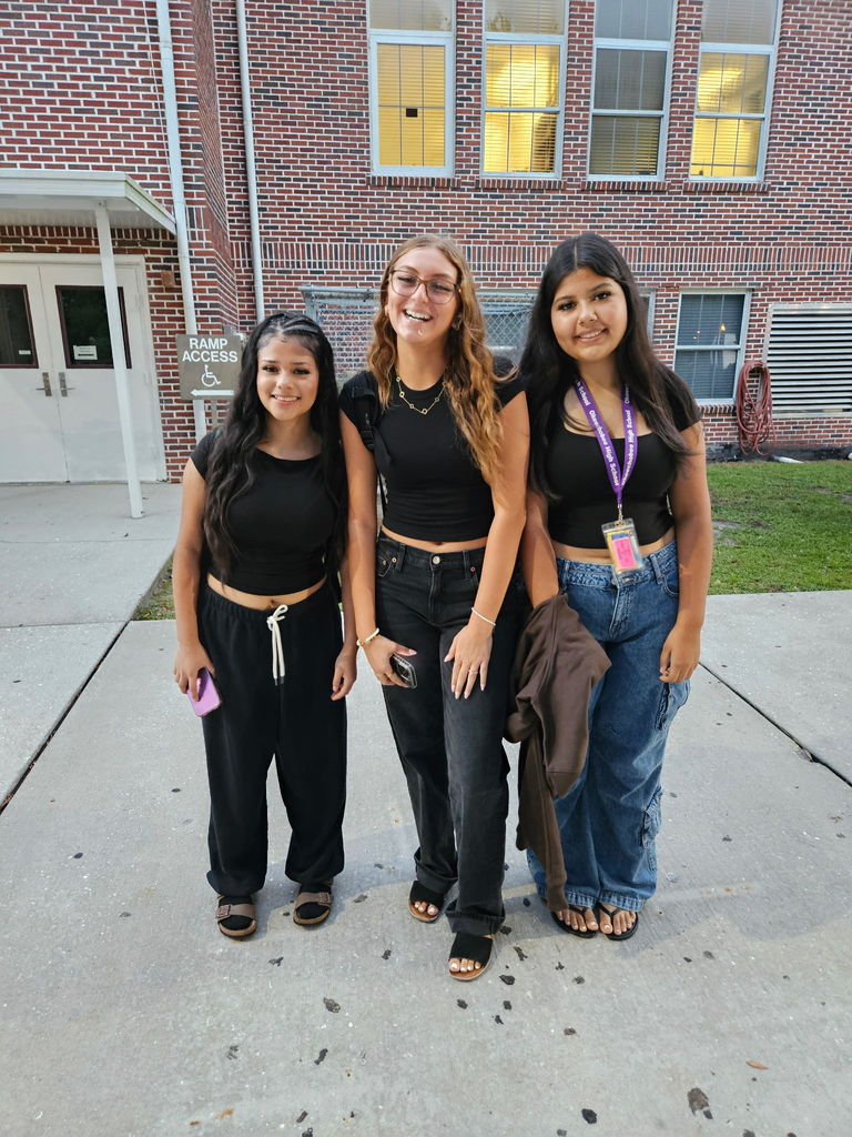three girls wearing black standing in school courtyard