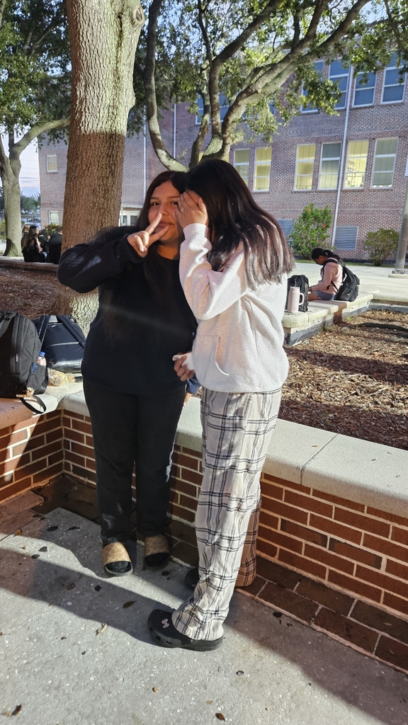 two girls standing in school courtyard one is covering her face and one with peace sign