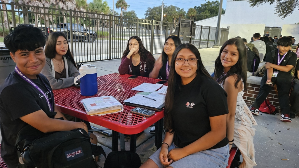 six students sitting in table in school courtyard