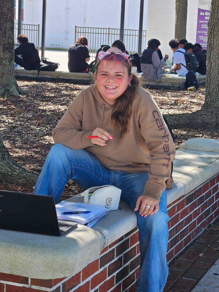 student sitting outside wearing pink glasses on her head