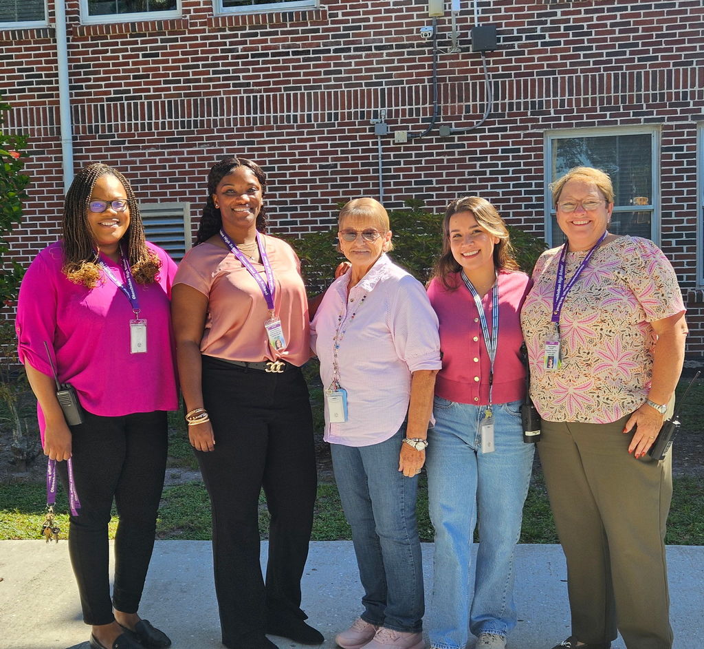 five school staff members wearing pink outside in school courtyard