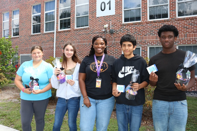 four students standing with prizes with guidance counselor outside of school