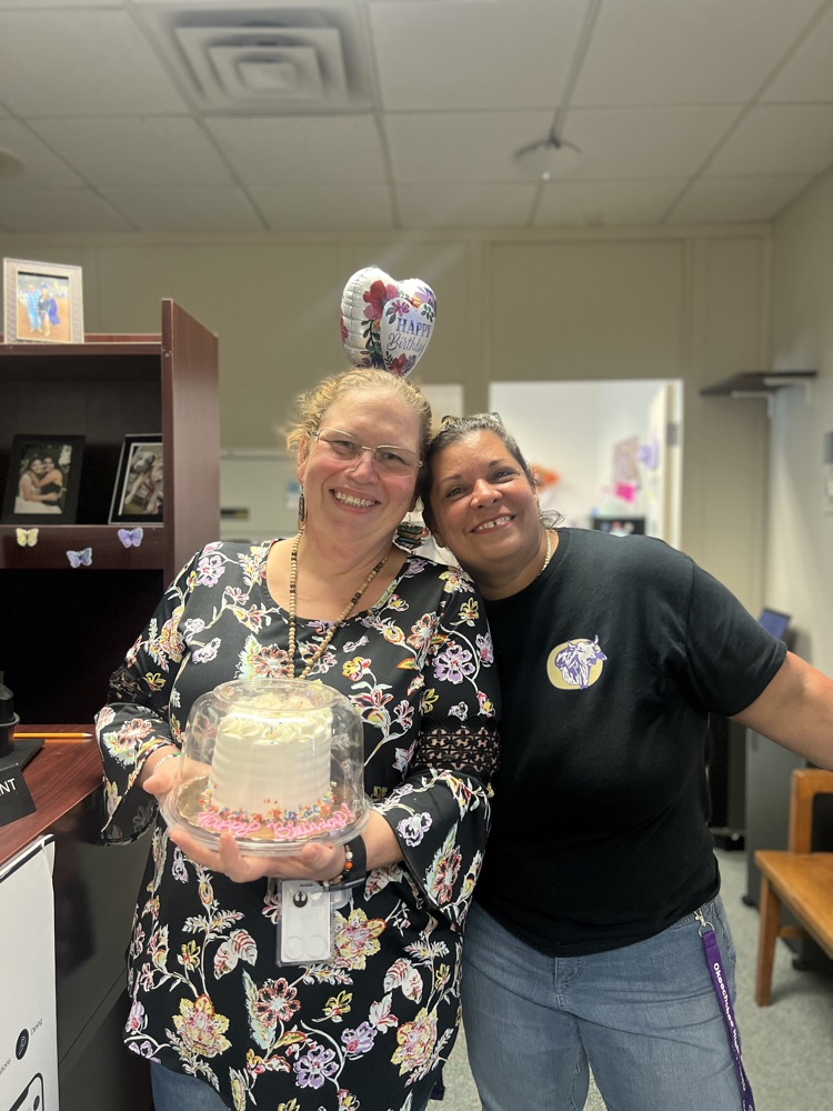 two teachers hugging each other holding a cake