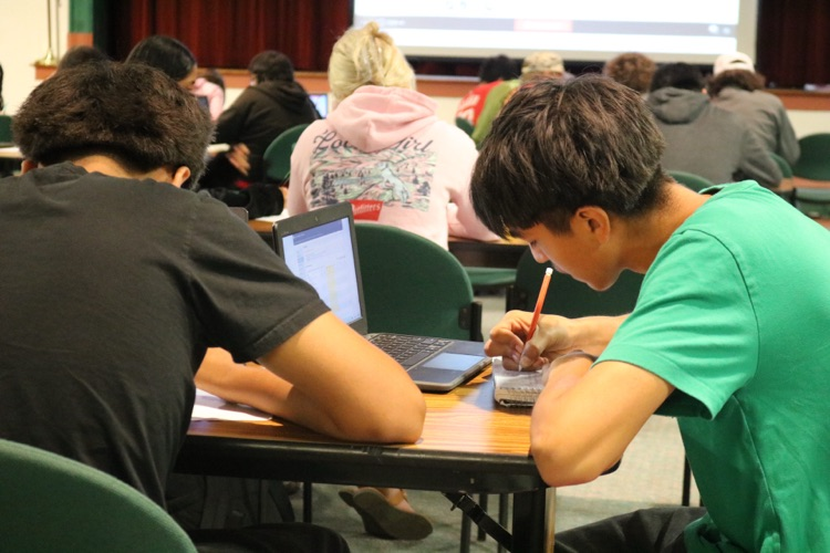 students writing down and looking at computers