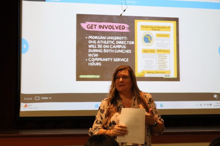 teacher speaking to auditorium about club