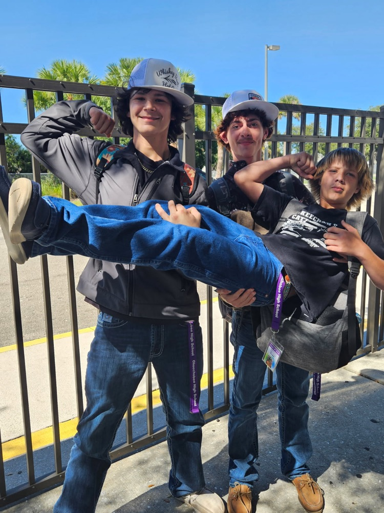 two students carrying another male student In courtyard