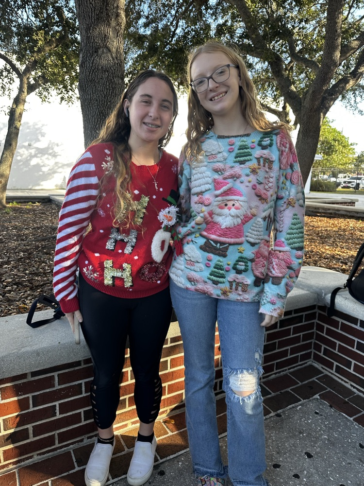 two students wearing ugly Christmas sweaters in school courtyard 