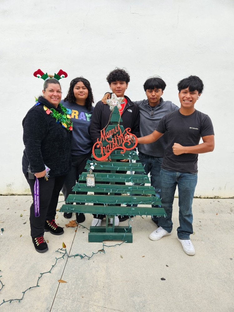 four students standing by Christmas tree and custodian outside