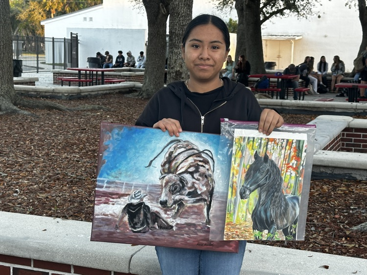 student showing two art pieces in courtyard