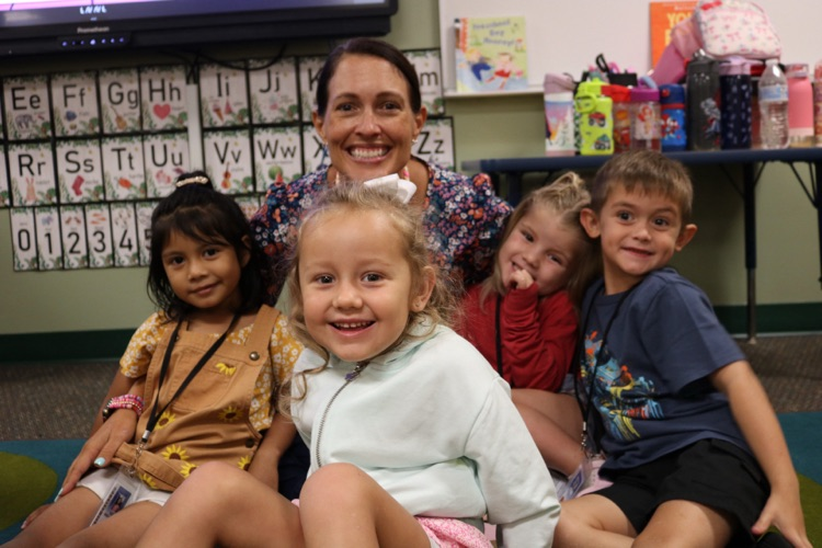 teacher hugging four students on carpet
